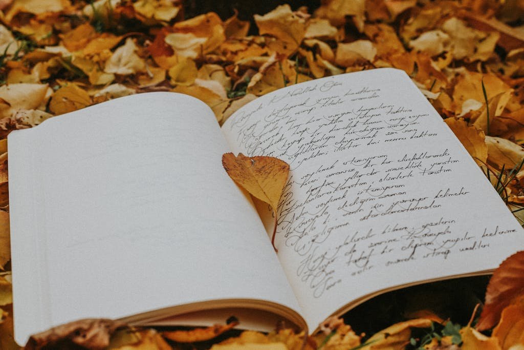 Open journal with cursive writing amidst vibrant autumn leaves.